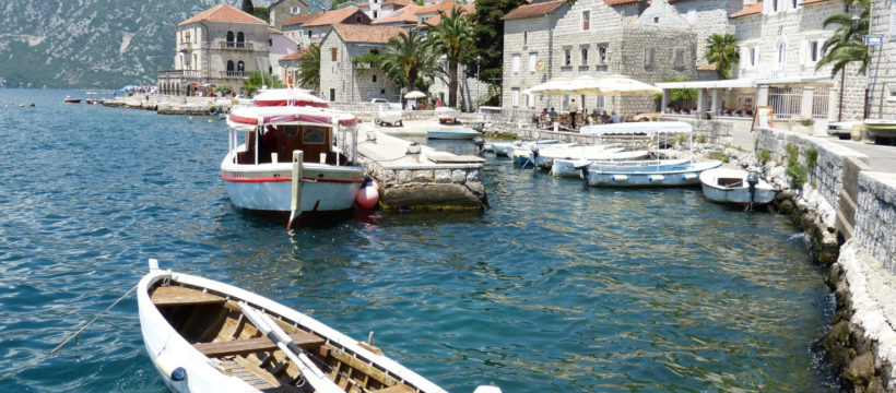 Bucht von Kotor, Fischerboote, blaues Wasser, weiße Steinhäuser, Berge am Ufer, blauer Himmer